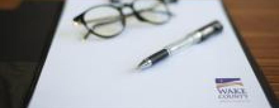 Glasses, a pen and Wake County letterhead rest on a table
