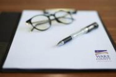 Glasses, a pen and Wake County letterhead rest on a table