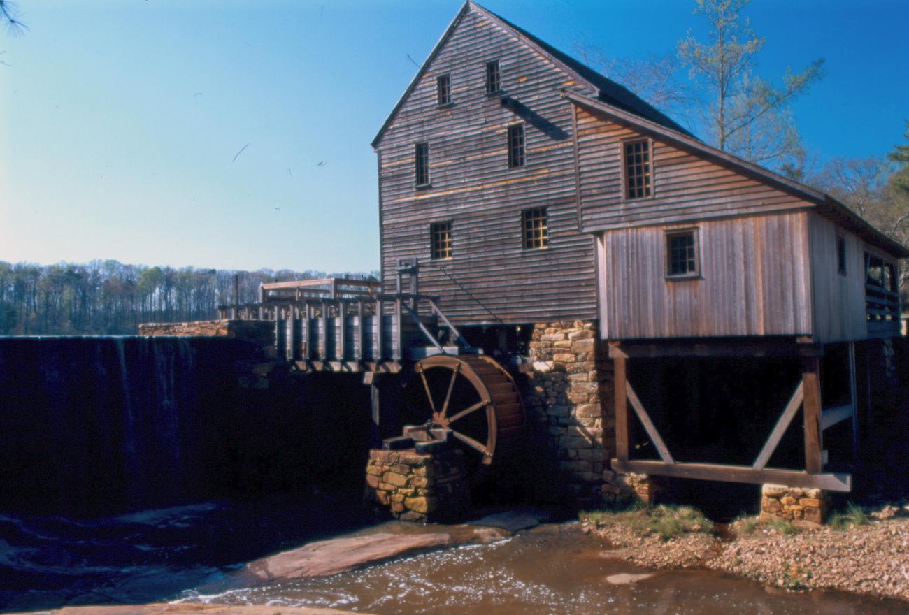 view of old historic wooden mill building with waterwheel beside of water dam