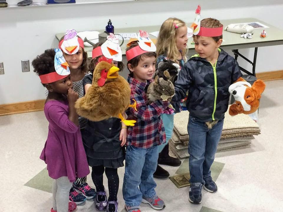group of children play with puppets and wear chick hats inside classroom