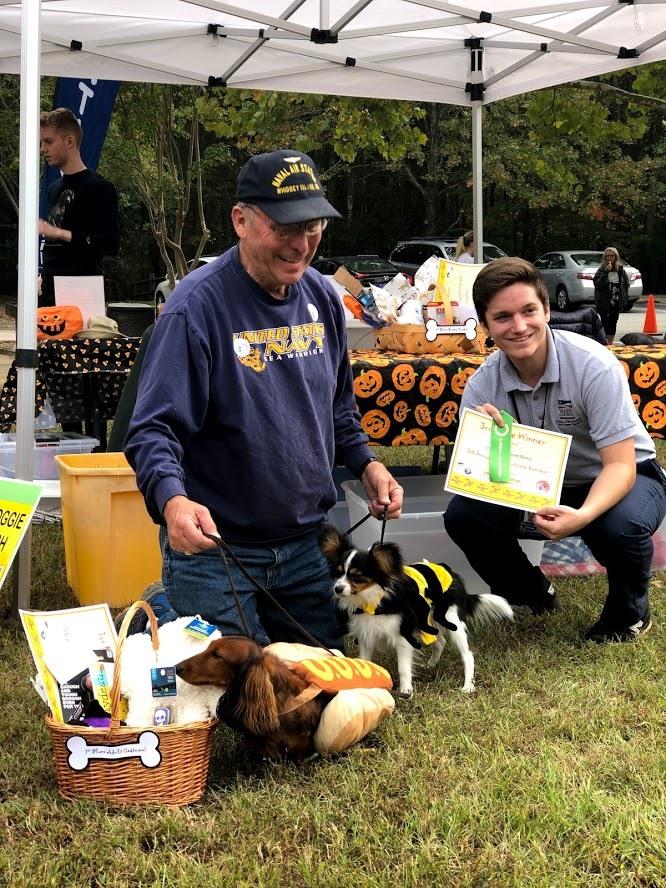 Man poses with park staff and two dogs in Halloween costumes to accept costume award