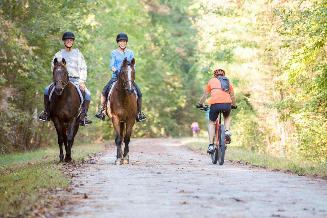 Two people riding horses and a person on a bicycle on the American Tobacco Trail