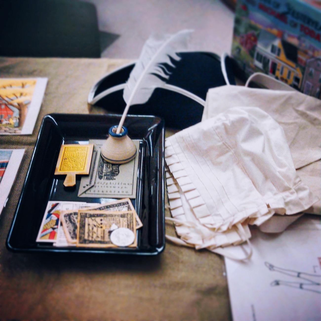 tray with old timey objects like feather pen, colonial money, and other replica items