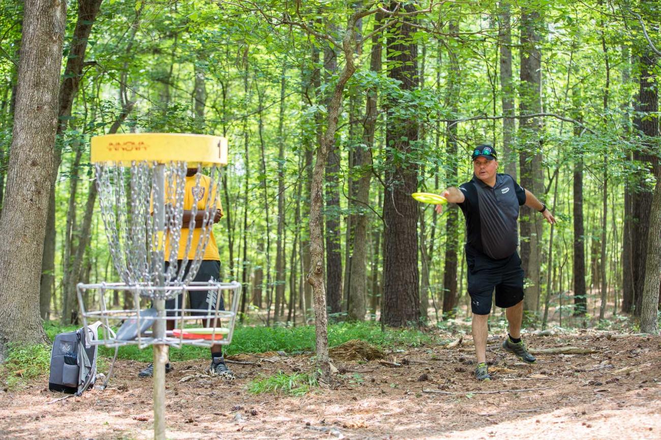 An individual playing the Buckhorn Disc Golf Course and throwing a disc at a basket