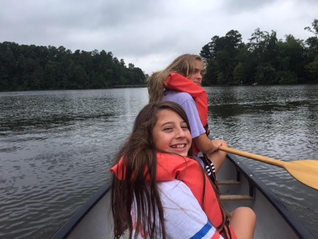 two girls look back at camera while on canoe on the pond