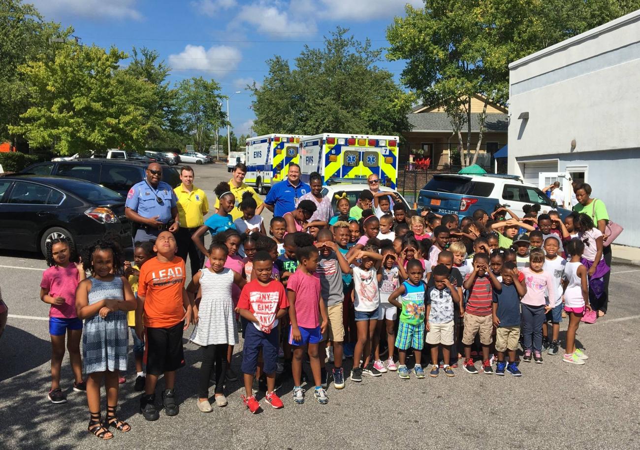 Many young children posing with paramedics in front of ambulances