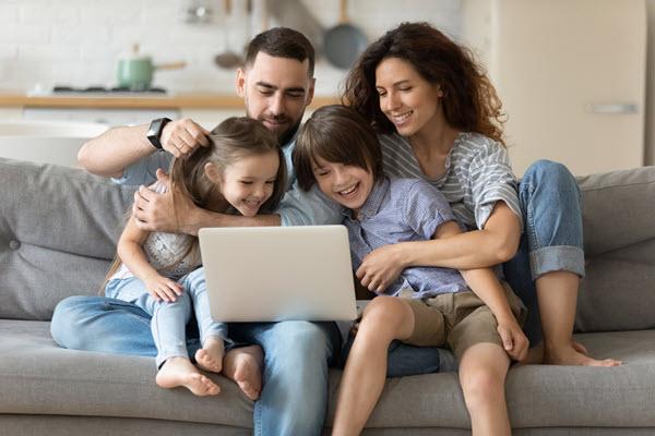 smiling family (mom, dad, boy, girl) sitting on the sofa looking at a laptop screen