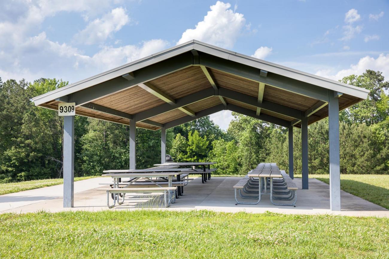Large, open-sided picnic shelter on concrete slab surrounded by green grass.