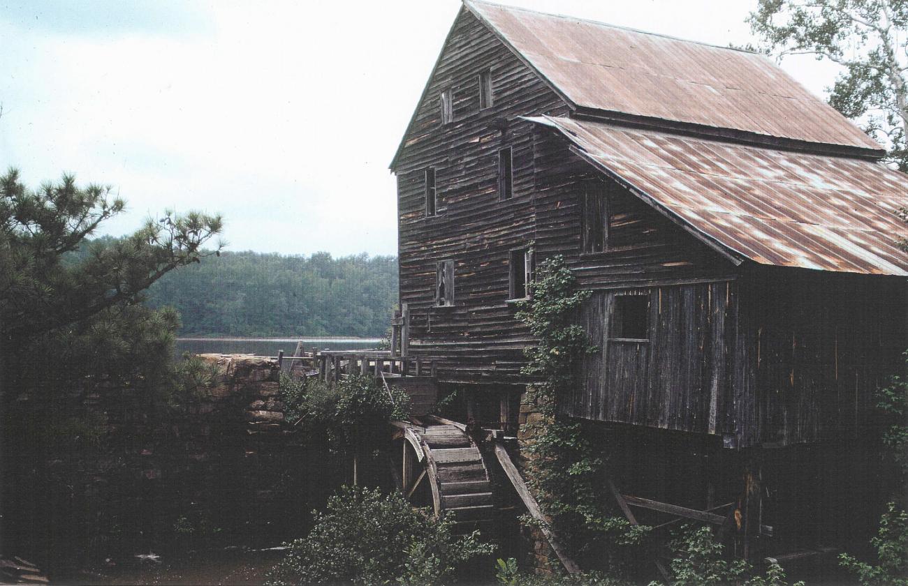 Old color photo of the mill before restoration, with ivy growing on the sides and parts falling apart