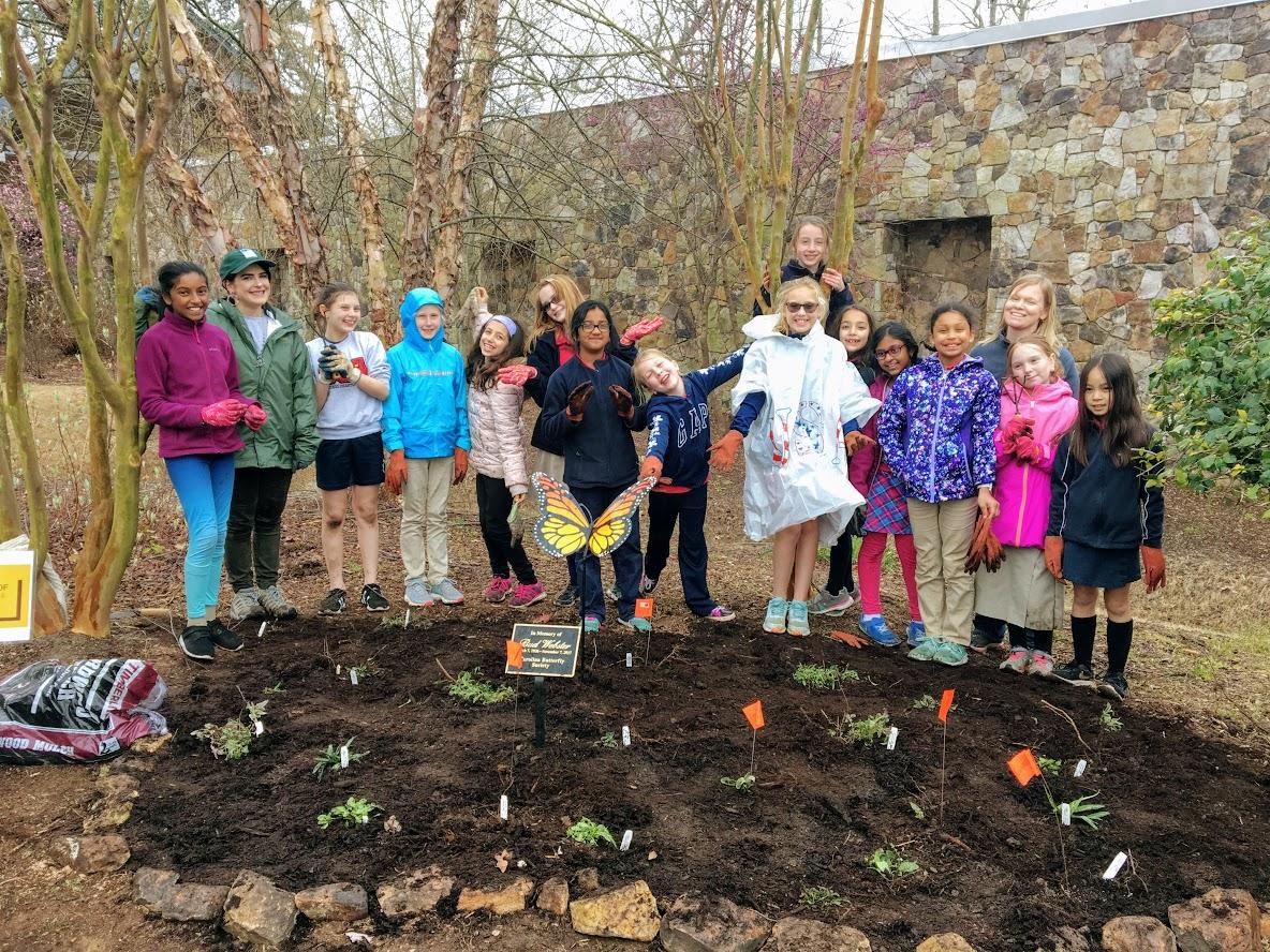 educator stands with group of girl scouts around a new flower bed with freshly planted flowers
