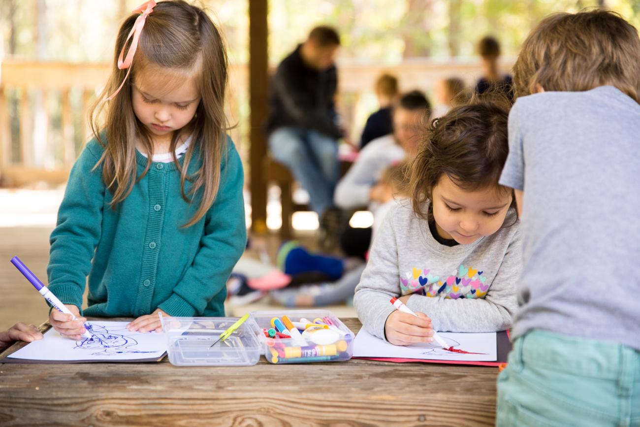 two girls color a craft together on a wooden bench