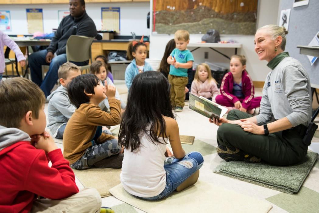 Educator sits on floor with group of children in classroom during storytime