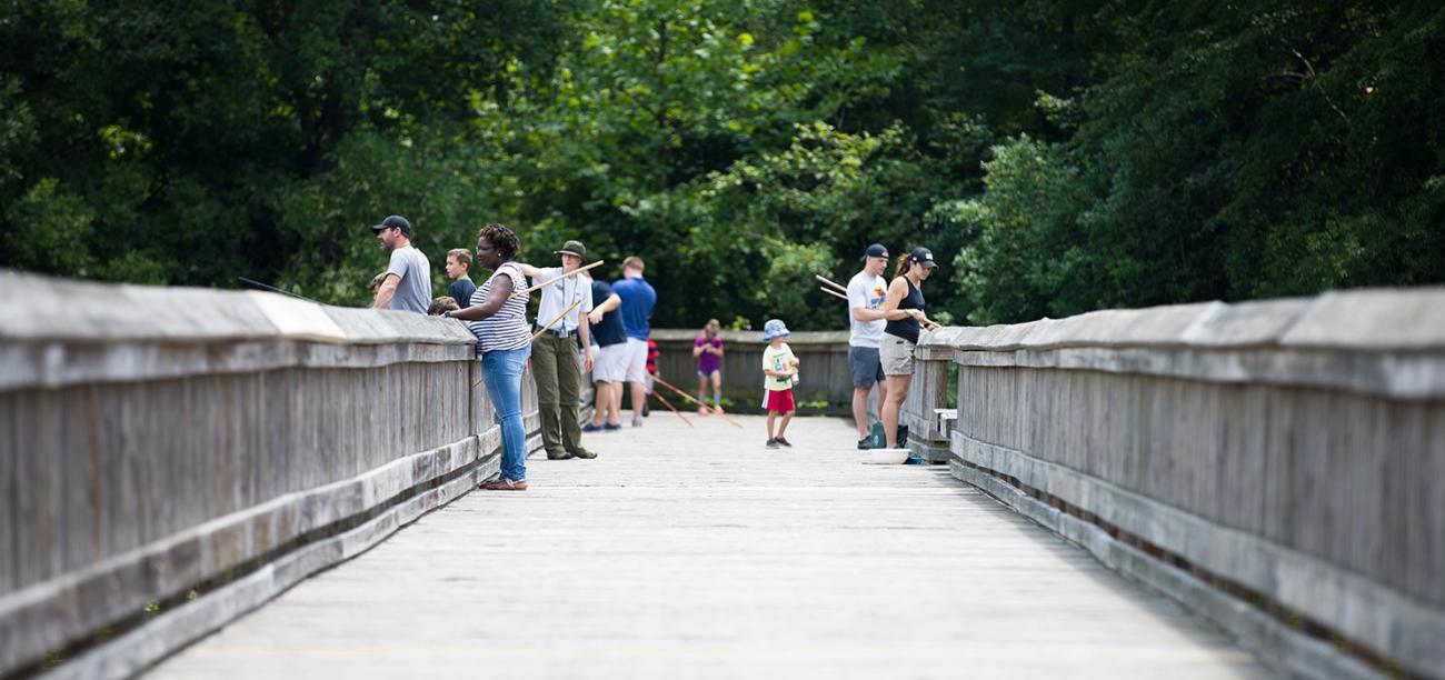 programmer teaches on wooden pond boardwalk while visitors fish with cane poles