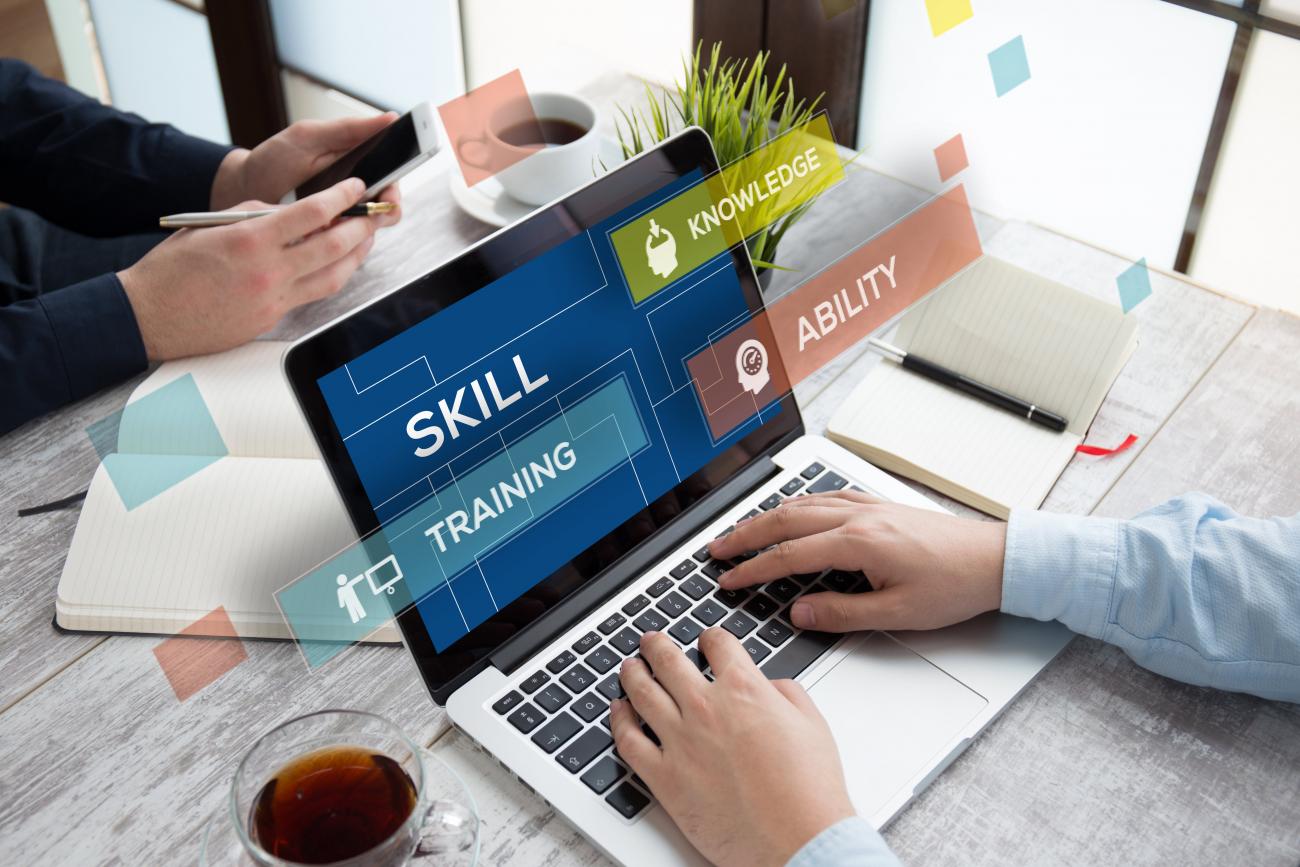 open laptop with the words skill, knowledge, training & ability on the screen, hands on the keyboard