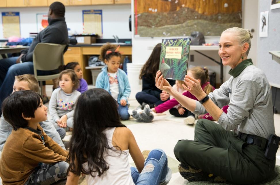Educator sits on floor with group of children in classroom during storytime