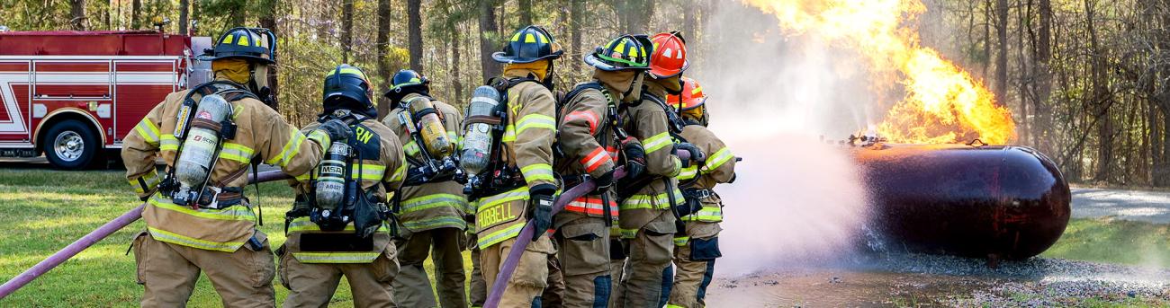 Fire trainees spray a hose on a burning storage tank