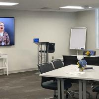 A picture of the Wake County Office Building Human Resources Training Room with tables & chairs, big screen monitor, and whiteboard