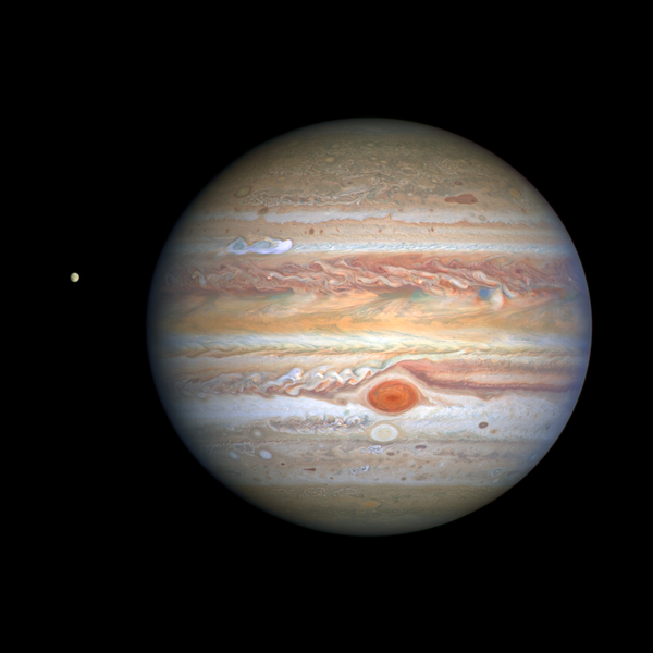 Image of Jupiter taken by the Hubble Space Telescope. The Great Red Spot is visible on the lower middle of the planet, and other turbulent layers can be seen in layers across the planet. The icy moon Europa can be seen to the left of Jupiter.
