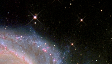 Cropped image of the edge of a galaxy, where the diffraction pattern can be seen on a few stars. The diffraction pattern looks like an 'X' shape.